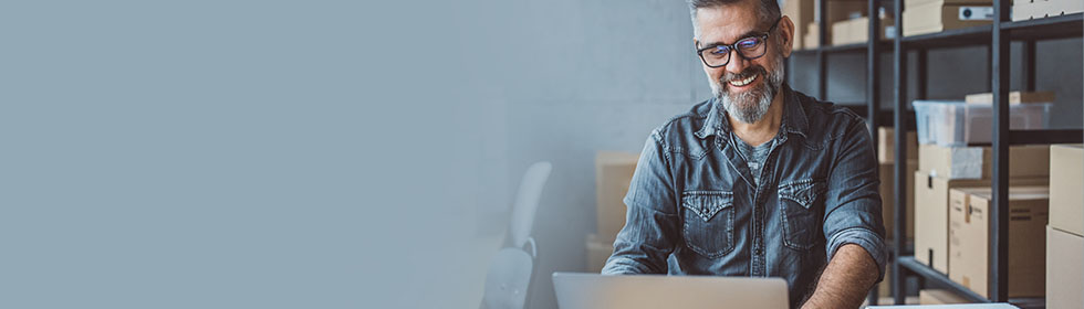 Geschäftsmann am Laptop vor vielen Paketen